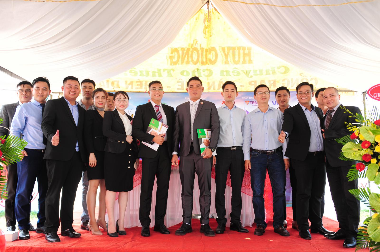 15 người đứng chụp ảnh trên bục trải thảm đỏ, mái che màu trắng