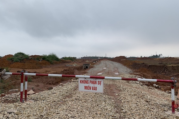 Doanh nghiệp địa ốc tạm dừng kế hoạch triển khai dự án. Barie chắn ngoài một khu đất trống có lối vào trải đá cuội.