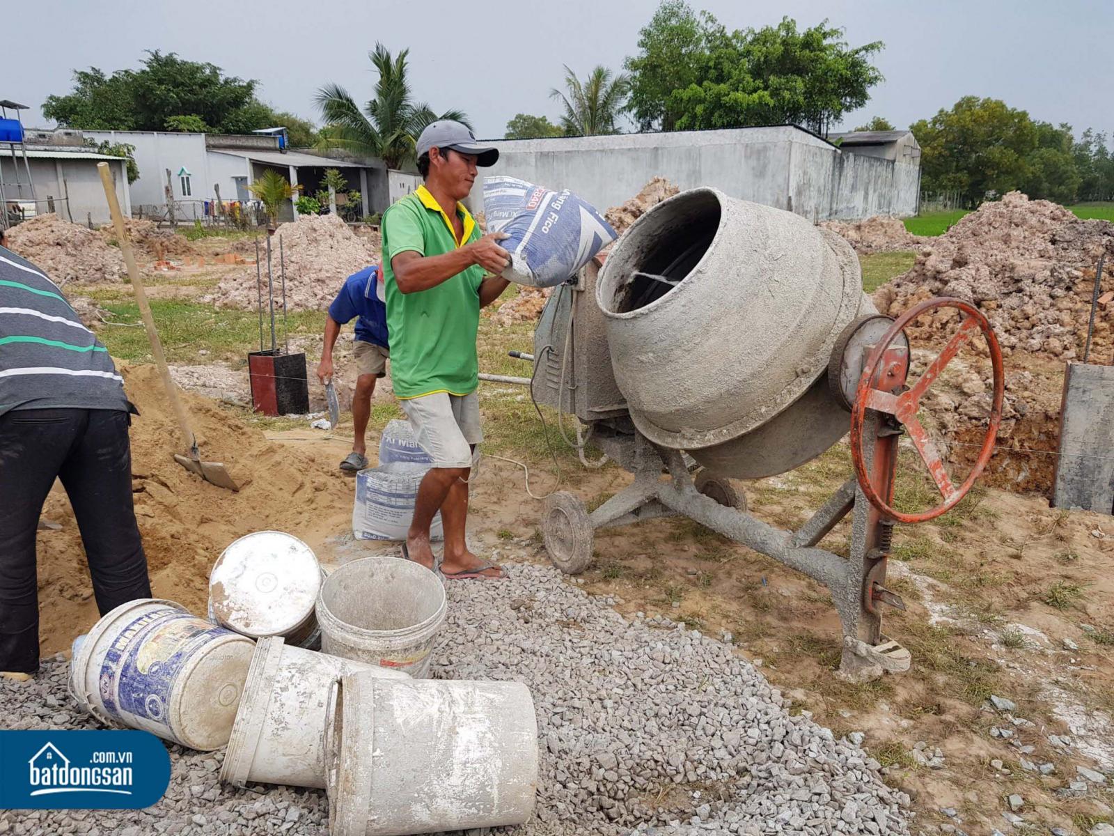 Ba nam công nhân đang đổ vật liệu vào máy trộn bê tông làm hạ tầng trong một dự án đất nền.